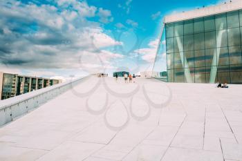 Oslo, Norway. The Groups Of People Going Up On The Slope Of Angled Roof Of Oslo Opera And Ballet House In Summer Day With Cloudy Sky.