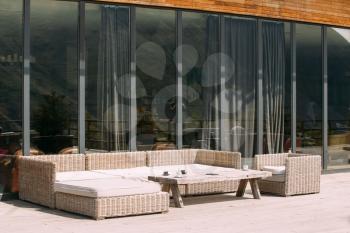 Wicker Furniture On Balcony At Sunny Summer Day. Home Exterior With Table, Chairs And Sofa In A Wooden Terrace
