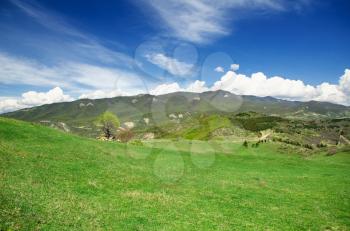 green meadow and mountains in the background of the beautiful blue sky with clouds