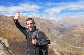 Happy tourist traveler with a black backpack in the mountains, smiling welcomes hand
