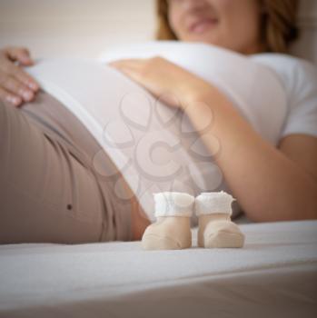 booties on a background of a pregnant woman lying on a bed