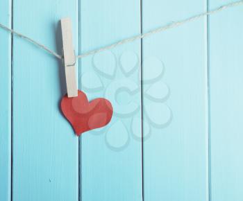 red heart made of paper with clothespin hanging on a rope and wooden blue  planks background with space for text