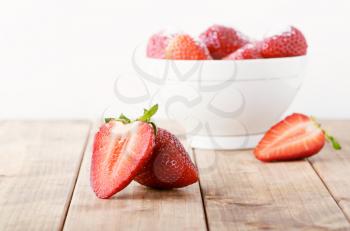 Juicy fresh cut strawberries in a white bowl on a wooden table background