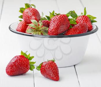 Ripe strawberries in a bowl on white wooden table
