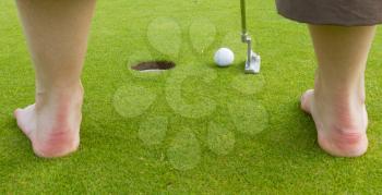 Golf player hitting the ball close-up on whole (barefoot)