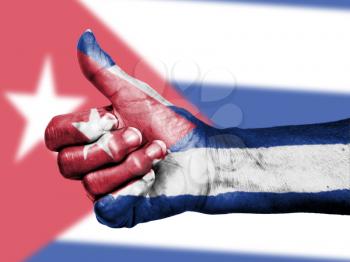 Old woman with arthritis giving the thumbs up sign, wrapped in flag pattern, Cuba