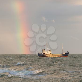 Small coastal vessel in the waters of the dutch Ijsselmeer, rainbow on the background