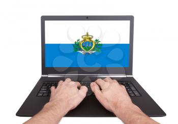 Hands working on laptop showing on the screen the flag of San Marino