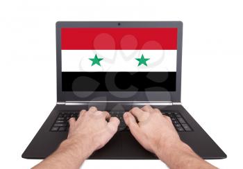 Hands working on laptop showing on the screen the flag of Syria