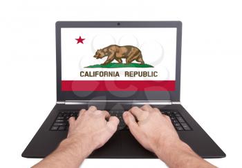 Hands working on laptop showing on the screen the flag of California
