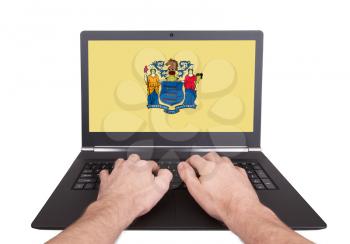 Hands working on laptop showing on the screen the flag of New Jersey