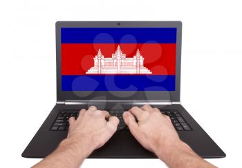 Hands working on laptop showing on the screen the flag of Cambodia