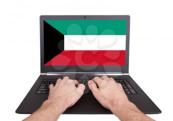 Hands working on laptop showing on the screen the flag of Kuwait