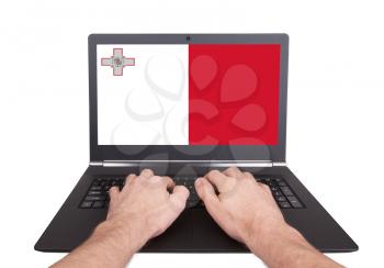 Hands working on laptop showing on the screen the flag of Malta