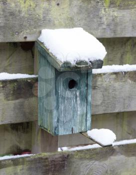 Birdhouse covert in snow, hanging on a wooden fence