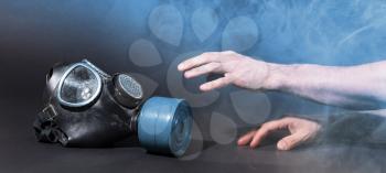 Man in room filled with smoke, trying to reach for vintage gasmask - Isolated on black - Blue smoke