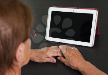 Senior lady relaxing and reading the screen of her tablet, black screen visible