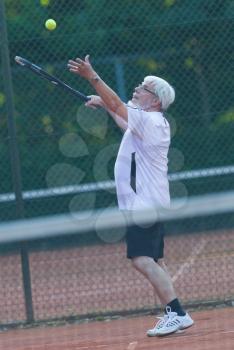 Senior man playing tennis on a gravel court