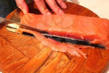 The image of hand cuts slices of a red fish