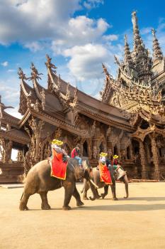 Tourists ride elephant around the Sanctuary of Truth in Pattaya, Thailand in a summer day