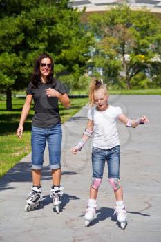 Learning mother and daughter on roller skates in summer
