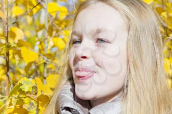 Autumn portrait of blond girl in sunlight put out tongue