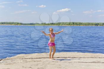 Dancing girl on the riverbank in pink swimsuit