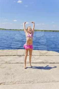 Cute jumping girl on the riverbank in pink swimsuit
