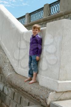 Cute boy with blond hair climbing on wall barefoot