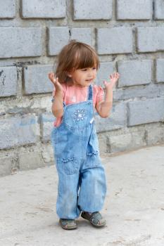 Cute baby girl with upward hands near the stone wall