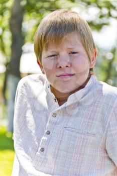 Portrait of  blond boy in a white shirt in green park
