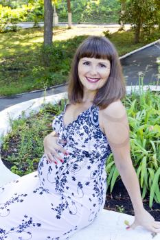 Smiling pregnant woman with brown hair sitting in summer