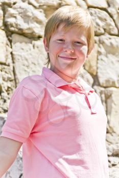 Smiling boy in pink shirt near stone wall
