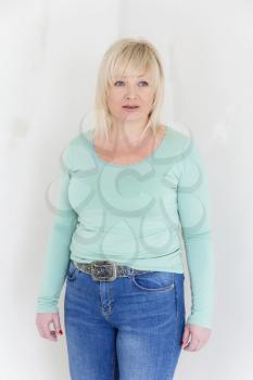 Blond woman in green and blue jeans stand on her knee inside empty room
