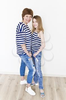 Happiest mother and daughter near white wall in striped clothes