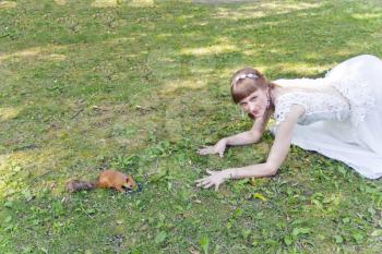 Bride in white lying on green grass next to the squirrel in summer