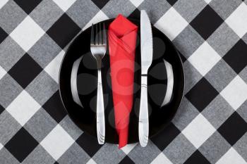 Black plate, fork and knife on plaid table cloth