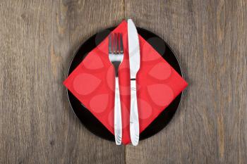Black plate, fork and knife on red napkin. 