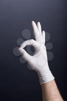 Male hand in latex glove (OK sign) on dark background