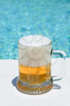 glass of cold beer on pool board in hot summer day 