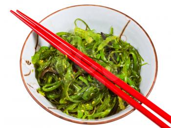 top view of chuka salad - seaweed salad sprinkled with sesame seeds in bowl with red chopsticks isolated on white background