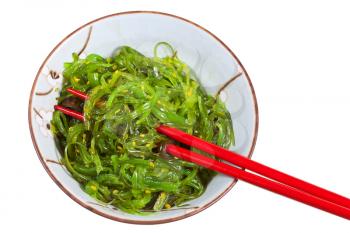 top view of seaweed salad in ceramic bowl with red chopsticks isolated on white background