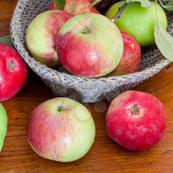 red and green apples in basket on wooden table close up