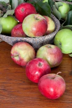 fresh apples with green leaves in basket on wooden table close up