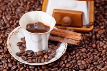 small cup of coffee and roasted coffee beans with old manual mill, cinnamon close up