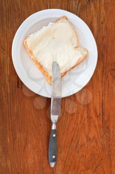 top view of bread and butter sandwich on white plate, knife on wooden table