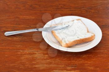 sandwich from toast and cottage cheese with herbs on white plate, table knife on wooden table