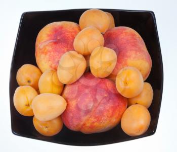 ripe peaches and apricots in black plate isolated on white background
