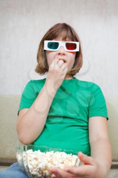 Girl watching TV movies in anaglyph 3D stereo glasses and eating popcorn