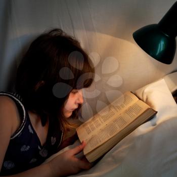 girl read book on bed at night by light of lamp on bed